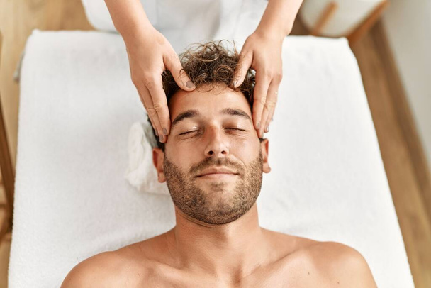 Joven hombre hispano teniendo masaje facial en el centro de belleza - Foto, imagen