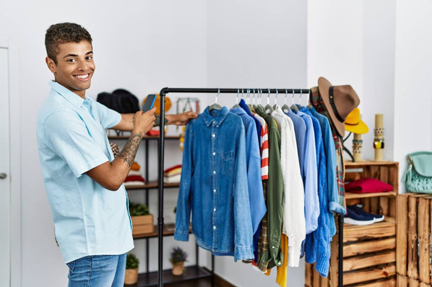 Joven hombre hispano de compras tomando fotos a la ropa en la tienda minorista - Foto, imagen