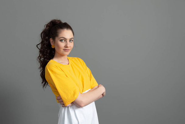 portrait of a young teenager with long wavy hair dressed in a yellow t-shirt, isolated on gray  - Fotó, kép