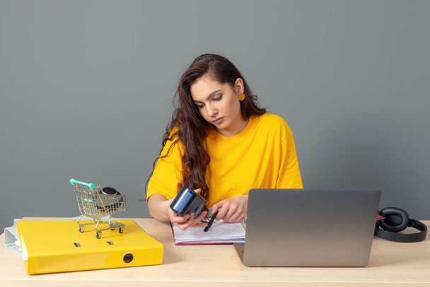 νεαρή επιχειρηματίας που κάθεται στο τραπέζι και εργάζεται με έγγραφα και φορητό υπολογιστή, απομονωμένη σε γκρι φόντο - Φωτογραφία, εικόνα