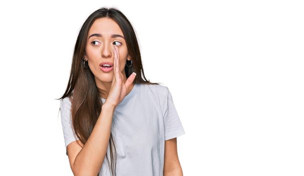 Young hispanic girl wearing casual white t shirt hand on mouth telling secret rumor, whispering malicious talk conversation  - Photo, image