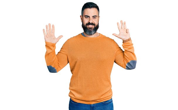 Hispanic man with beard wearing casual winter sweater showing and pointing up with fingers number nine while smiling confident and happy.  - Foto, afbeelding
