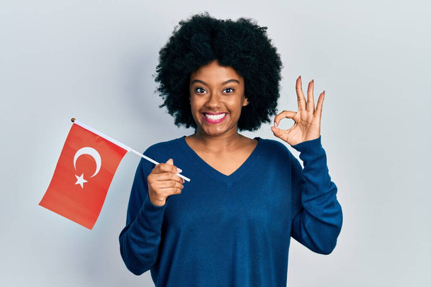 Nuori afrikkalainen amerikkalainen nainen tilalla kalkkuna lippu tekee ok merkki sormin, hymyillen ystävällinen ele erinomainen symboli  - Valokuva, kuva