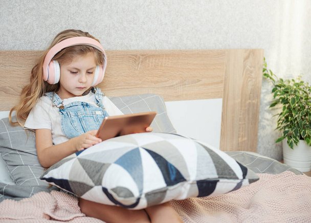Aranyos kislány fülhallgatóban tabletet használ otthon. - Fotó, kép