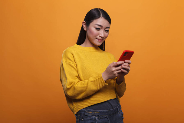 Pewna siebie uśmiechnięta Azjatka korzystająca z nowoczesnego smartfona do przeglądania Internetu. - Zdjęcie, obraz