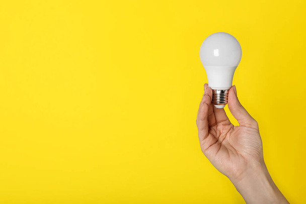 Woman holding LED light bulb on yellow background, closeup. Space for text - Foto, imagen