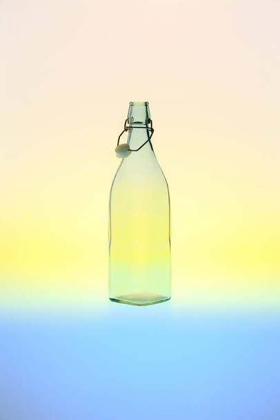 Vacío, botella de vidrio cuadrado vintage con un tapón superior de clip abierto contra el verano, fondo de degradado colorido - Foto, Imagen