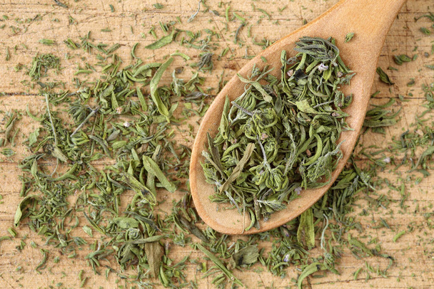 Top down view of dried summer savory in a wooden spoon, on a rustic wooden table. Close up of chopped, dry Satureja hortensis, a culinary and medicinial herb, with selective focus - Photo, Image