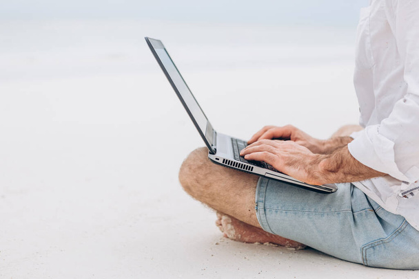 Человек руки печатает текст на ноутбуке компьютера перед синим морем на пляже Thw. Концепция удаленной работы, фрилансер. - Фото, изображение