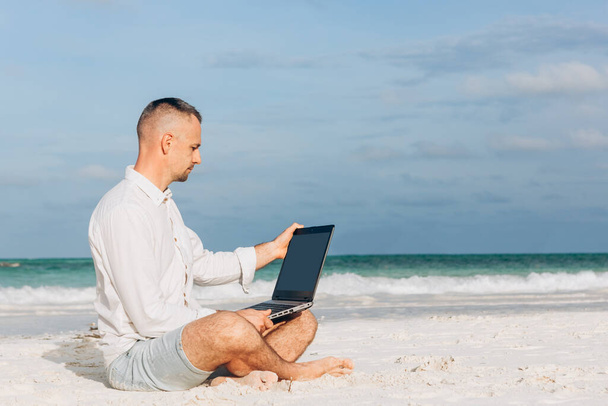 Młody człowiek korzystający z laptopa na plaży. Relaks Urlop Praca na świeżym powietrzu Beach Concept - Zdjęcie, obraz