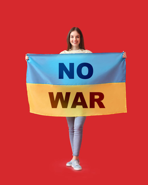 Молодая женщина, держащая украинский флаг с текстом NO WAR на красном фоне  - Фото, изображение