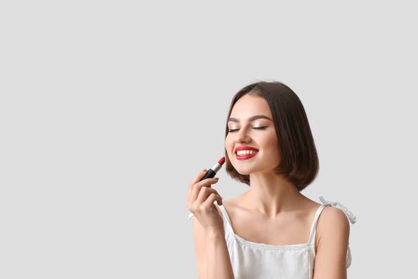 Happy woman with closed eyes holding red lipstick on light background - Photo, Image