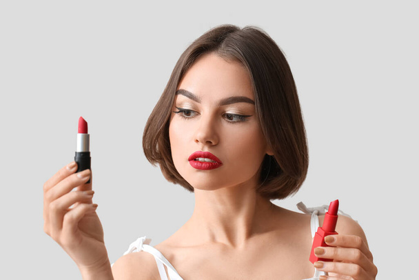 Beautiful woman holding red lipsticks on light background - Photo, Image