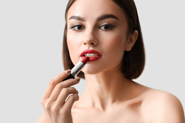 Hermosa mujer aplicando lápiz labial rojo sobre fondo claro - Foto, imagen