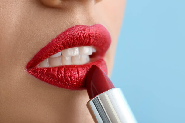 Vrouw die rode lippenstift op kleur achtergrond, close-up - Foto, afbeelding