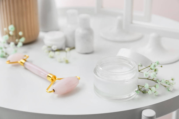 Tarro de producto cosmético, herramienta de masaje facial y flores en la mesa, primer plano - Foto, Imagen