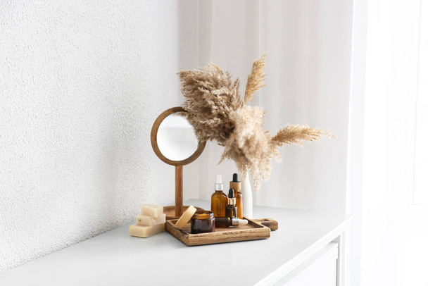 Holzbrett mit Kosmetik, Spiegel und Pampasgras auf der Kommode im Zimmer - Foto, Bild