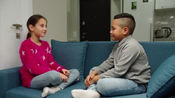Multiethnische Kinder spielen, gestikulieren, High Five sitzen drinnen auf dem Sofa - Filmmaterial, Video