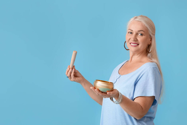 Mature woman with Tibetan singing bowl on color background - Foto, afbeelding