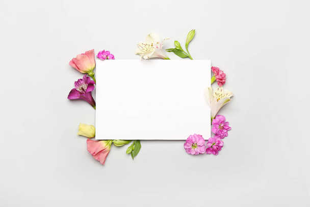 Πλαίσιο από διαφορετικά λουλούδια και λευκή χάρτινη κάρτα σε λευκό φόντο - Φωτογραφία, εικόνα