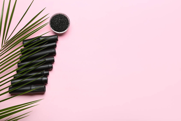 Bowl of activated carbon powder, black bamboo sticks and palm leaf on color background - Photo, Image