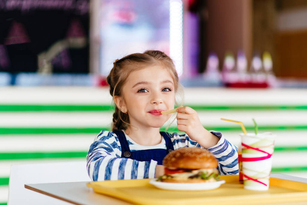 little girl eating a hamburger in outdoor cafe - Foto, Imagen