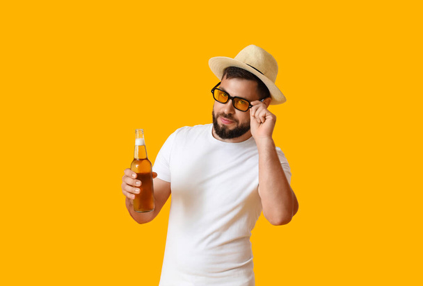 Young man in sunglasses with bottle of beer on yellow background - Foto, Imagem