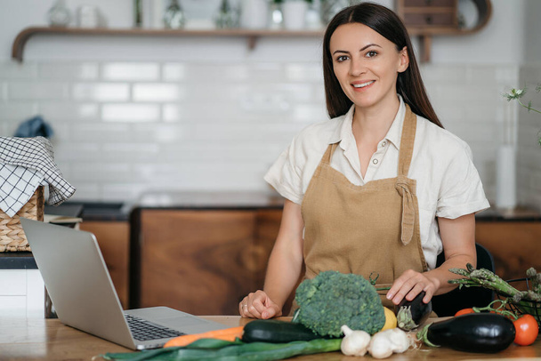 vrouw met laptop tijdens het koken van groenten - Foto, afbeelding