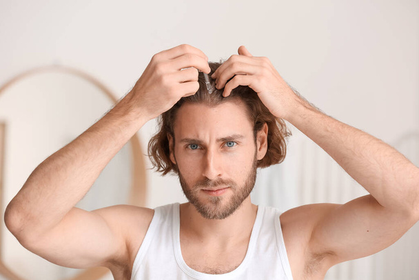 Молодий чоловік використовує сироватку для росту волосся у ванній
 - Фото, зображення