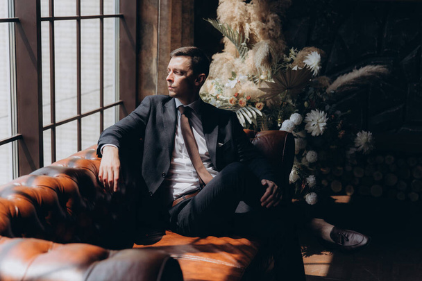 Morning of a stylish groom, man, in a black suit and tie, his preparations at the hotel, in a photo studio, fastening buttons and jacket, portraits - Photo, image