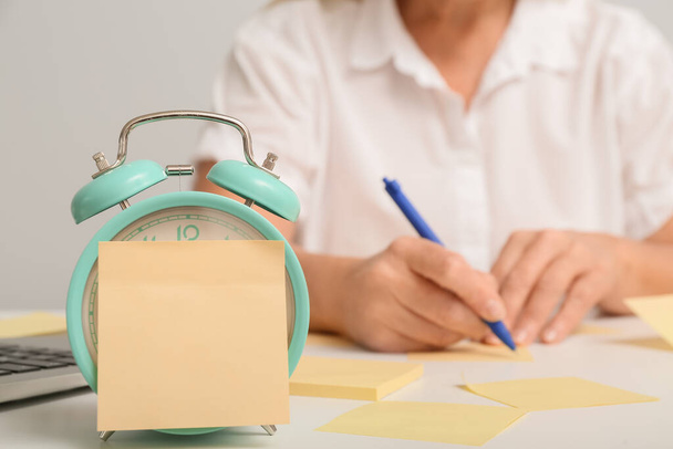 Будильник и липкие бумажки на столе зрелой женщины - Фото, изображение