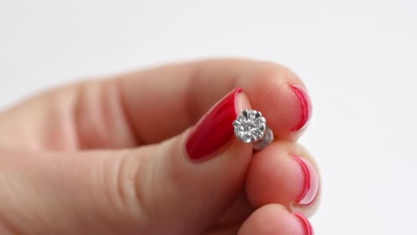 ダイヤモンドでイヤリングを保持する女性の近くのビュー。白い背景、赤い爪の手 - 映像、動画