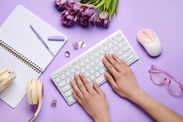 Kobiece ręce z klawiaturą, kwiaty, akcesoria i notatnik i tło liliowe - Zdjęcie, obraz