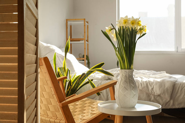Vaas met verse narcissen bloemen op tafel in gezellige slaapkamer - Foto, afbeelding