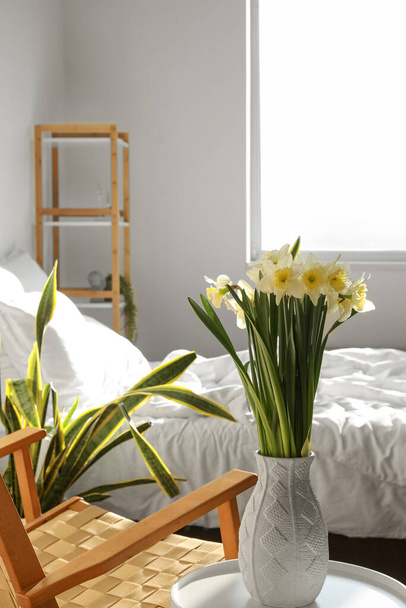 Vaas met verse narcissen bloemen op tafel in gezellige slaapkamer - Foto, afbeelding