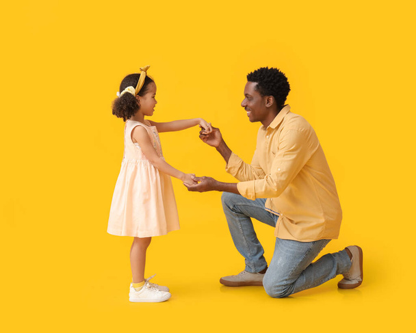 Μικρό Αφροαμερικανό κορίτσι και ο πατέρας της σε κίτρινο φόντο - Φωτογραφία, εικόνα