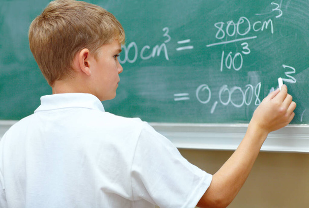 Είναι μια μικρή ιδιοφυΐα. Νεαρός μαθητής κάνει μια εξίσωση στον πίνακα στο σχολείο. - Φωτογραφία, εικόνα