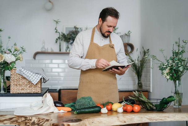 Schöner Mann mit grünen Zutaten und würzigen Kräutern bereitet in der Küche gesundes Essen zu - Foto, Bild