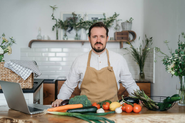 Yeşil malzemeleri ve baharatlı otları olan yakışıklı bir adam mutfakta sağlıklı yemek hazırlıyor. - Fotoğraf, Görsel