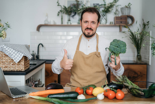 Όμορφος άντρας με πράσινα υλικά και πικάντικα βότανα που ετοιμάζει υγιεινό φαγητό στην κουζίνα - Φωτογραφία, εικόνα