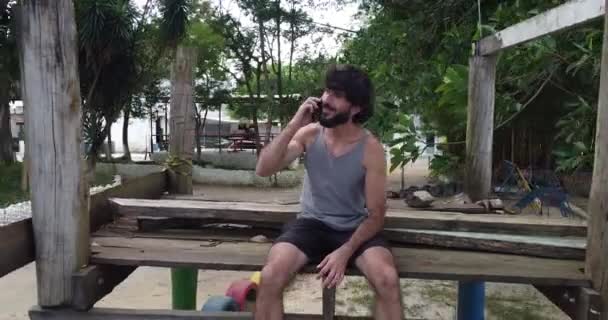 młody człowiek korzystający ze smartfona w dzień z zielonym parkiem w tle - Materiał filmowy, wideo