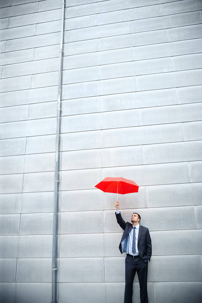 Raising his cover - Insurance. A young businessman holding a red umbrella while outdoors. - Photo, Image