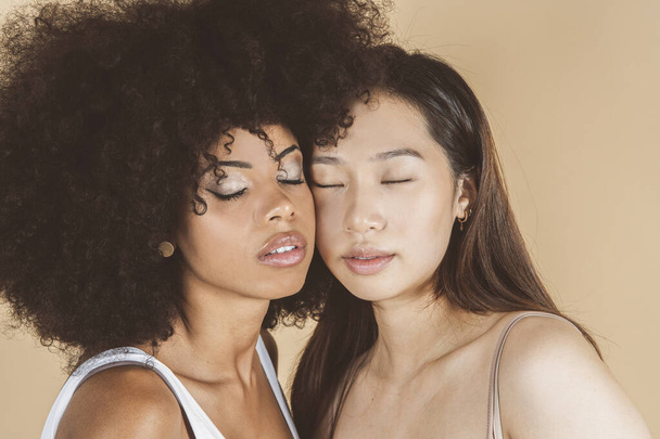 Twee jonge diverse vrouwen in ondergoed staan op beige achtergrond close-up, ogen dicht - Foto, afbeelding