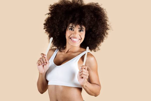 Afroamerikanerin mit Zahnbürste glücklich lächelnd, Studio braunen Hintergrund - Foto, Bild