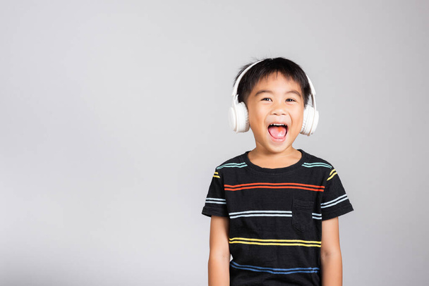 Little cute kid boy 5-6 years old listen music in wireless headphones in studio shot isolated on white background, happy Asian children smiling listening audio, entertainment lifestyle - Photo, Image