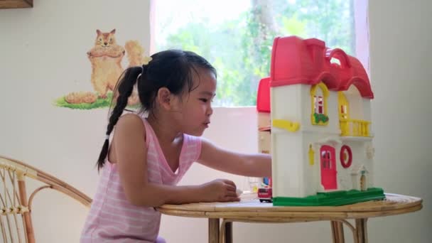 Šťastná holčička hrající si s plastovou panenkou dům s mini nábytkem hračky a panenka. Roztomilá holčička v růžových šatech se těší v dětském pokoji - Záběry, video