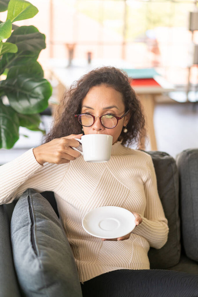 Латинська жінка п "є каву на дивані в домашньому фільтрі. - Фото, зображення