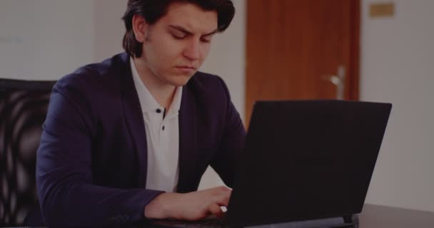 Τεταμένος νεαρός επιχειρηματίας που χρησιμοποιεί φορητό υπολογιστή στο γραφείο - Πλάνα, βίντεο