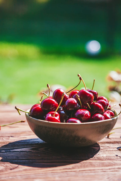 A bowl with fresh, ripe and tasty cherry on a table standing outdoors - Foto, Imagem