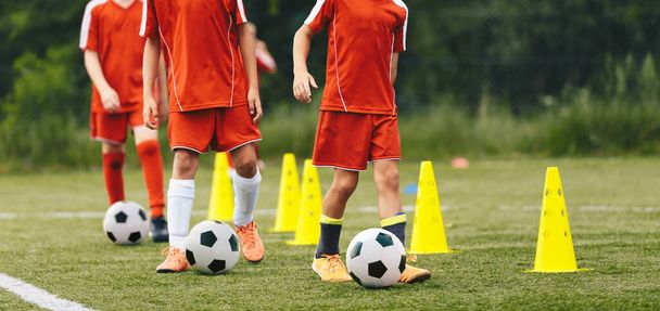 Egy csapat fiatal fiú focizik a fociedzéseken. Futball csöpögő gyakorlatok. A gyerekek golyókkal szaladgálnak a sárga gyakorlóbóják között. Három focibarát, akik továbbképzésben részesülnek - Fotó, kép